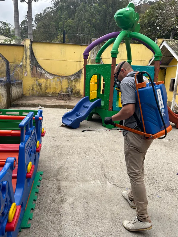 Técnico da Ecolife com pulverizador costal aplicando produto em parquinho escolar